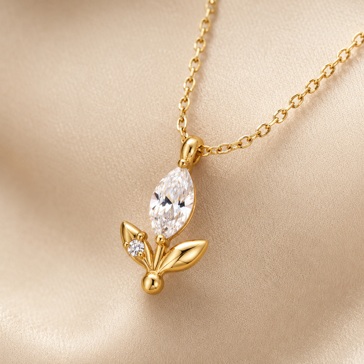 Gold pendant necklace featuring a marquise-cut clear crystal and a small round clear stone, displayed on a soft beige satin background.