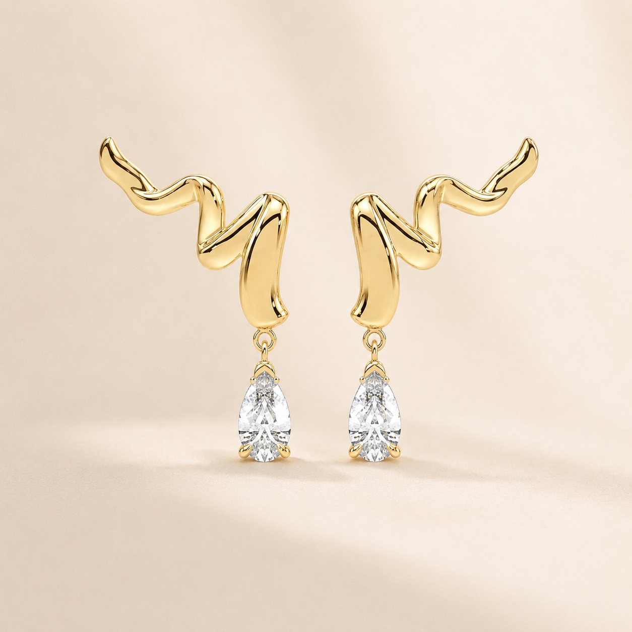 A pair of gold dangle earrings with abstract wavy post designs and clear teardrop-shaped gemstones, shown on a soft beige background.