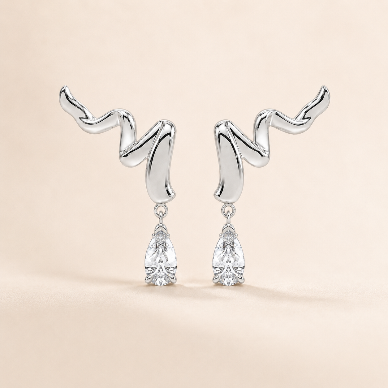 A pair of silver drop earrings with abstract, wavy curved tops and clear teardrop-shaped gemstones hanging below, set against a soft beige background.
