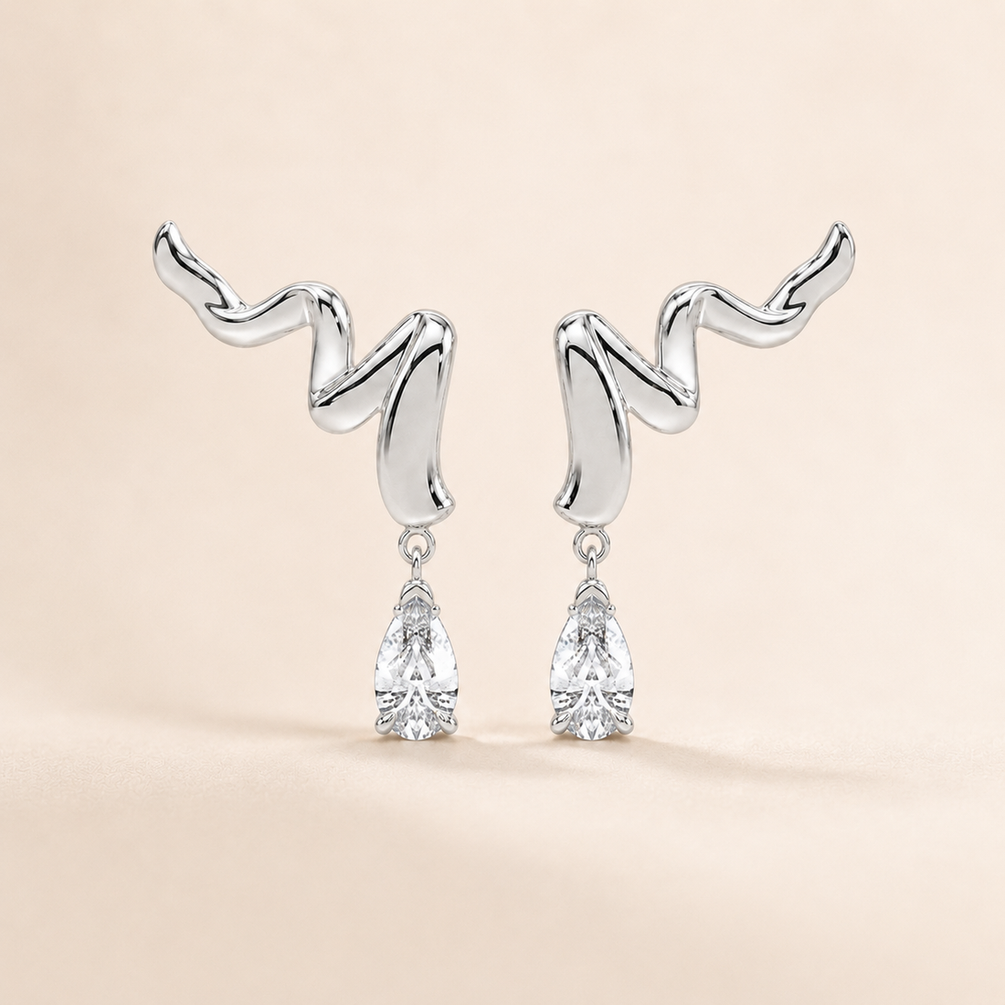 A pair of silver drop earrings with abstract, wavy curved tops and clear teardrop-shaped gemstones hanging below, set against a soft beige background.