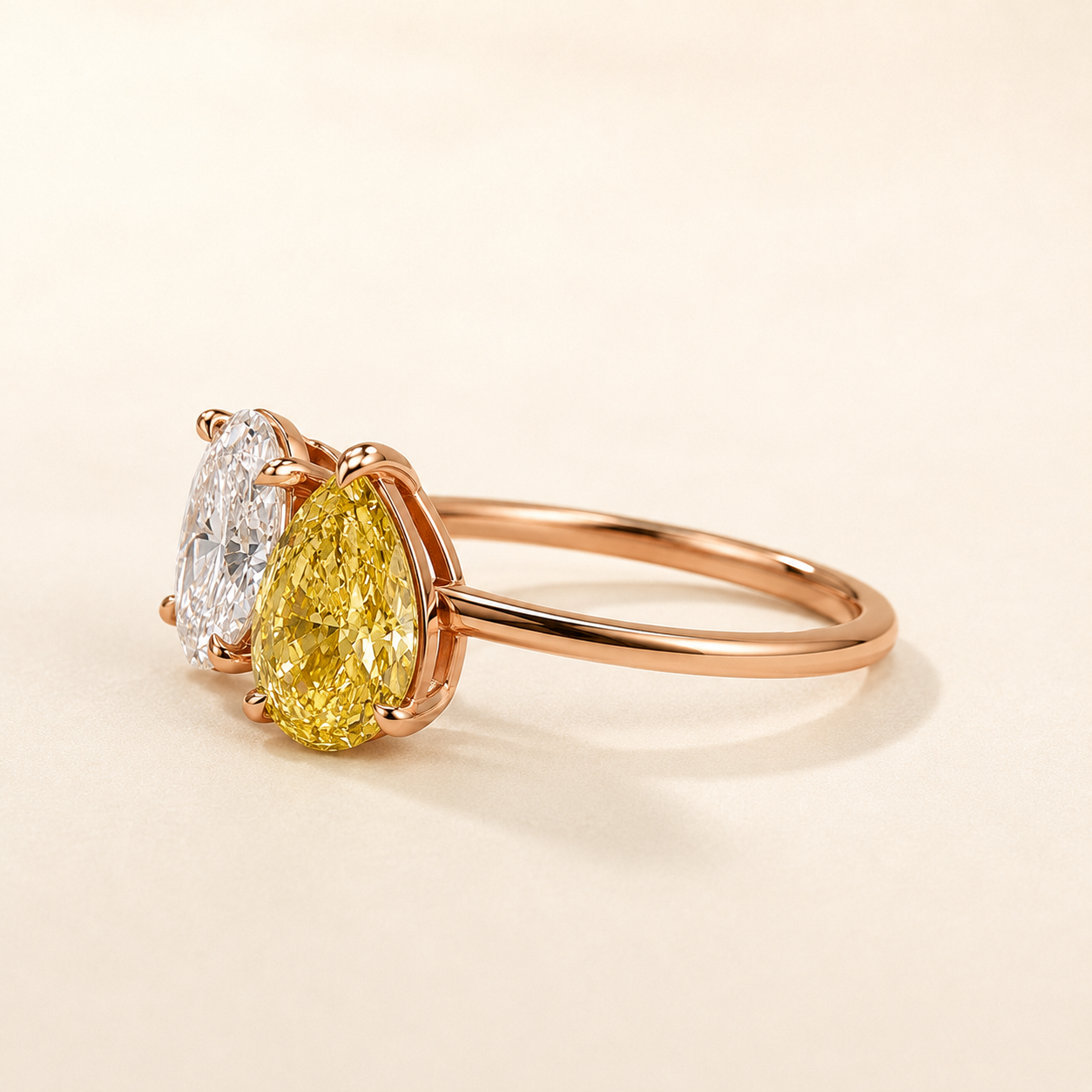 A rose gold ring featuring a pear-cut yellow diamond and a round brilliant-cut white diamond, set on a warm cream background.