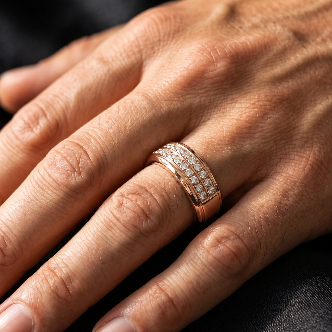 A close-up of a hand wearing a rose gold ring set with small clear stones in a double row on the ring finger.