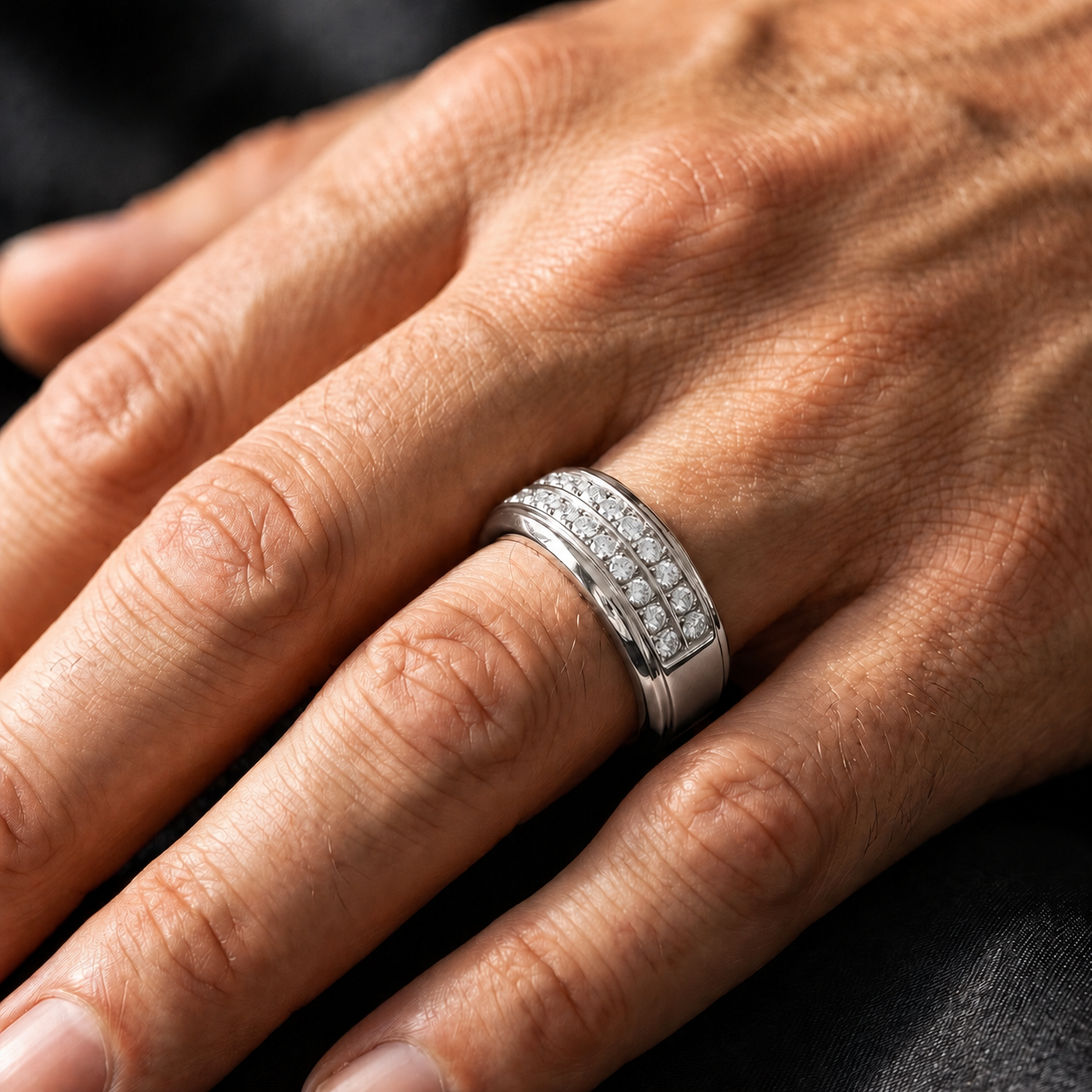 A close-up of a hand wearing a silver band ring set with small clear stones on the ring finger, against a dark background.