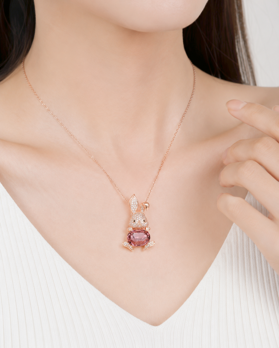 A close-up of a model wearing a delicate rose gold necklace with a rabbit-shaped pendant featuring a pink gemstone.