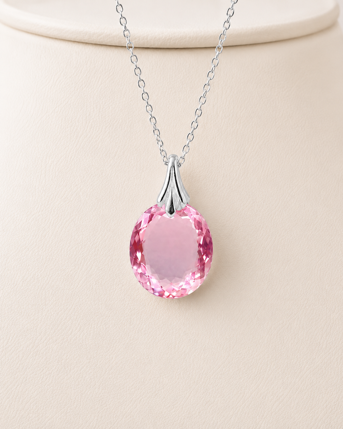 A silver pendant necklace with a faceted pink teardrop gemstone, displayed on a cream-colored jewelry bust.