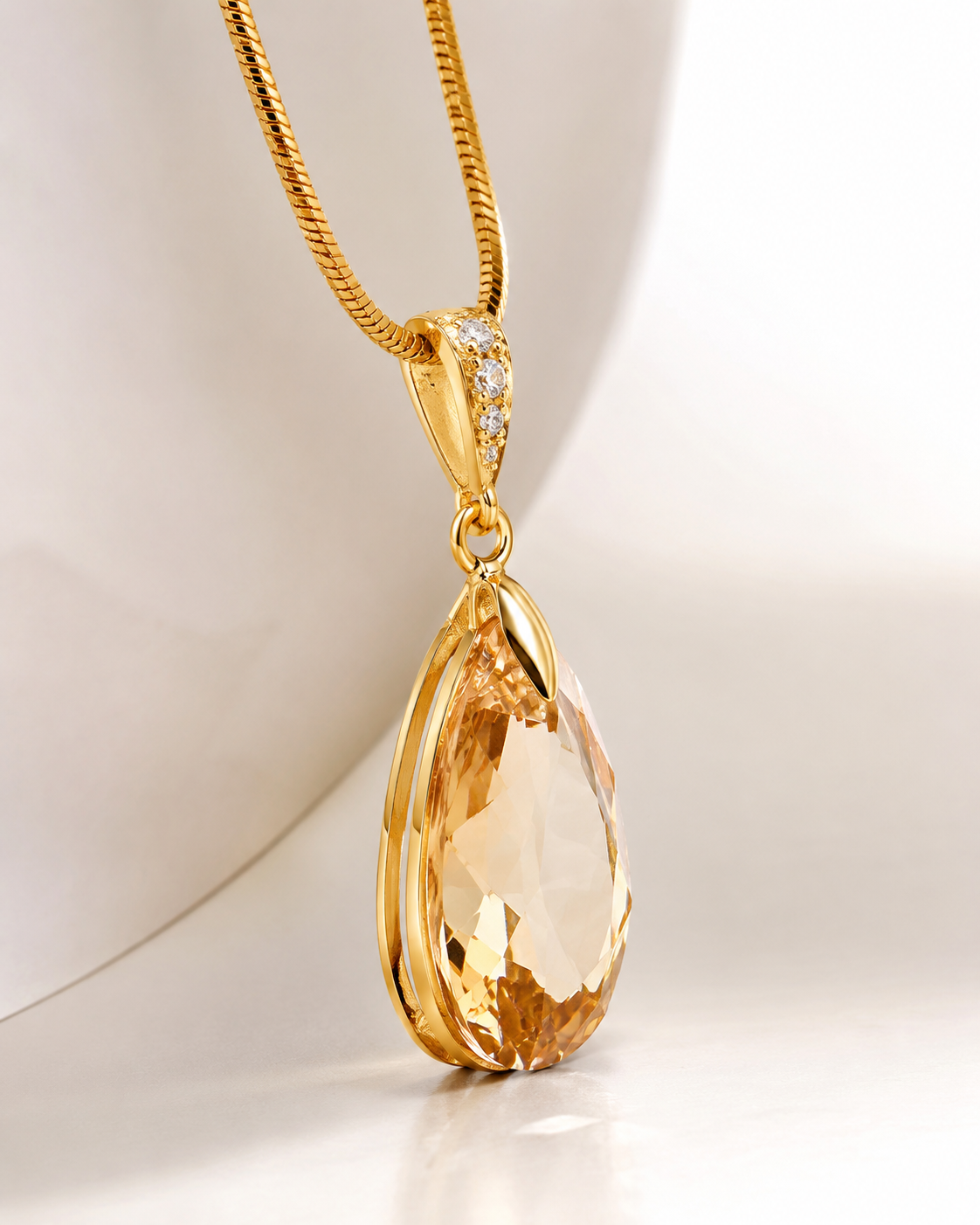 A gold teardrop pendant necklace with a faceted amber gemstone and a small diamond-accented bail, displayed on a white curved mannequin bust.