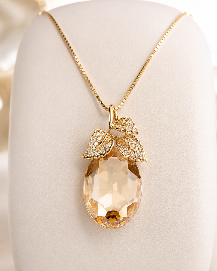 Gold leaf pendant necklace with a large faceted peach crystal and pavé crystal leaves, displayed on a cream jewelry bust.