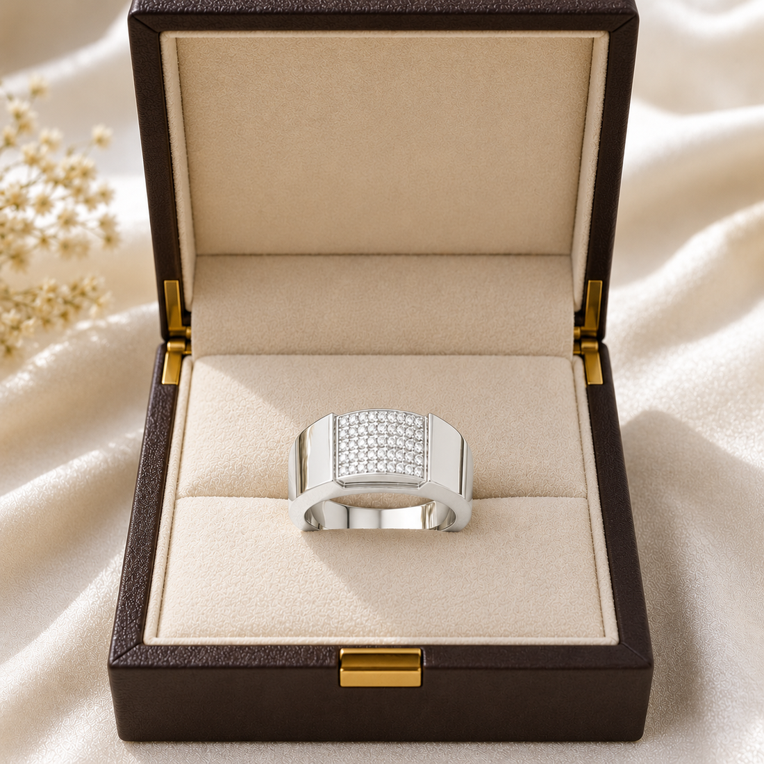 A silver-toned men's ring with a square pavé-set crystal face, displayed inside an open dark brown jewelry box with a beige velvet lining.