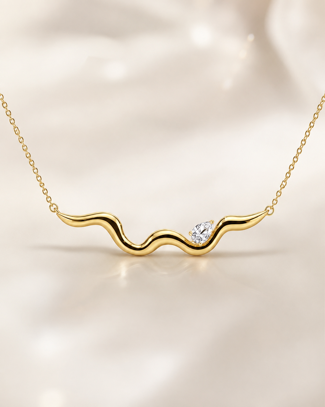 A gold wavy necklace with a small clear heart-shaped gemstone, displayed on a soft, light beige fabric background.