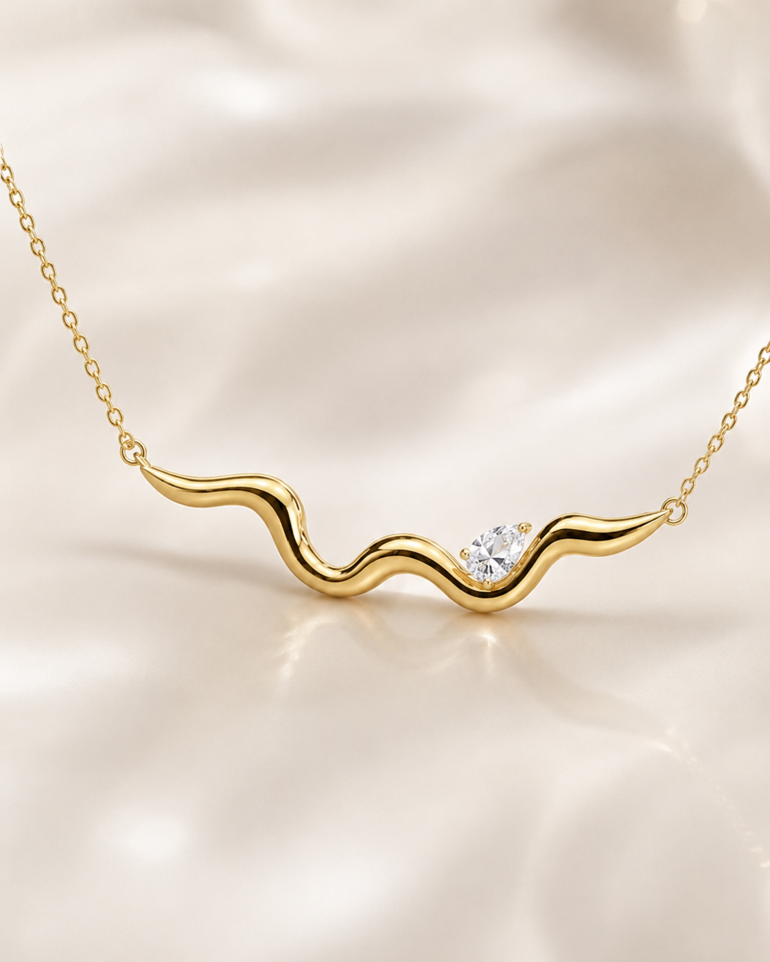 A gold wavy necklace with a small clear gemstone, displayed on a soft, draped cream satin fabric background.