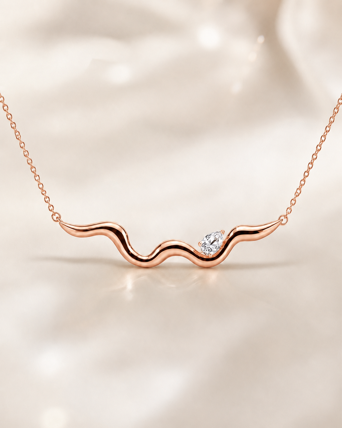 A rose gold wavy necklace with a small clear heart-shaped gemstone, displayed on a soft, light beige fabric background.