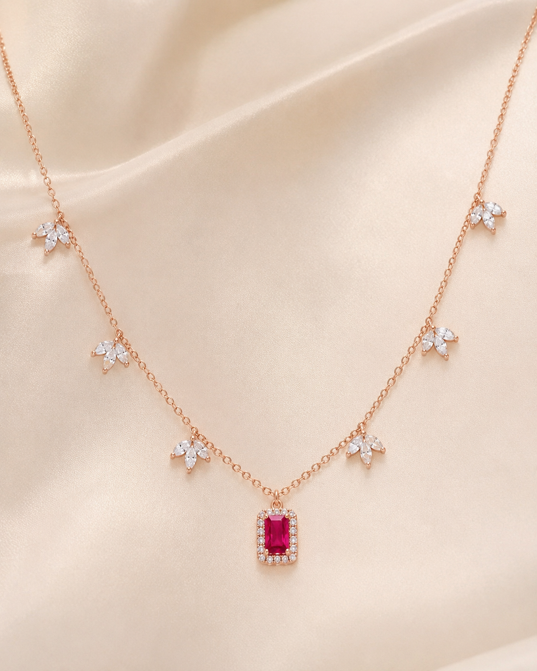 Rose gold necklace with a rectangular pink gemstone pendant and five small star-shaped floral clusters on a champagne satin background.