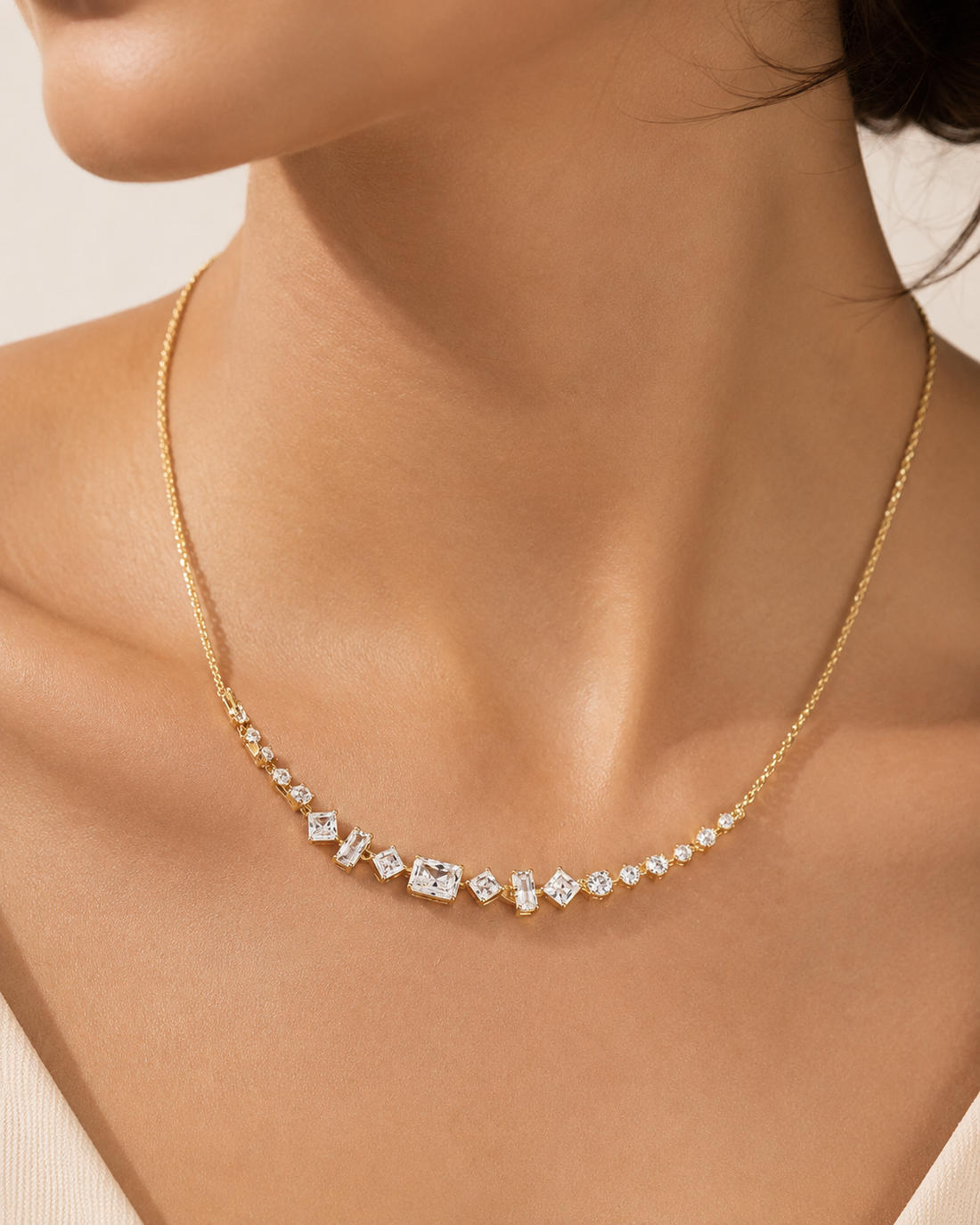 A delicate gold chain necklace with a curved row of clear gemstones, worn on a model's neck.
