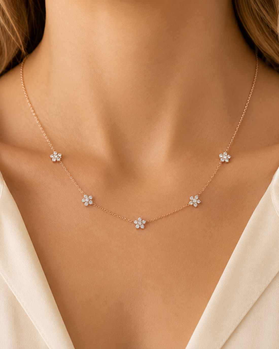A delicate rose gold necklace with five small flower-shaped charms, worn by a model in a close-up shot.