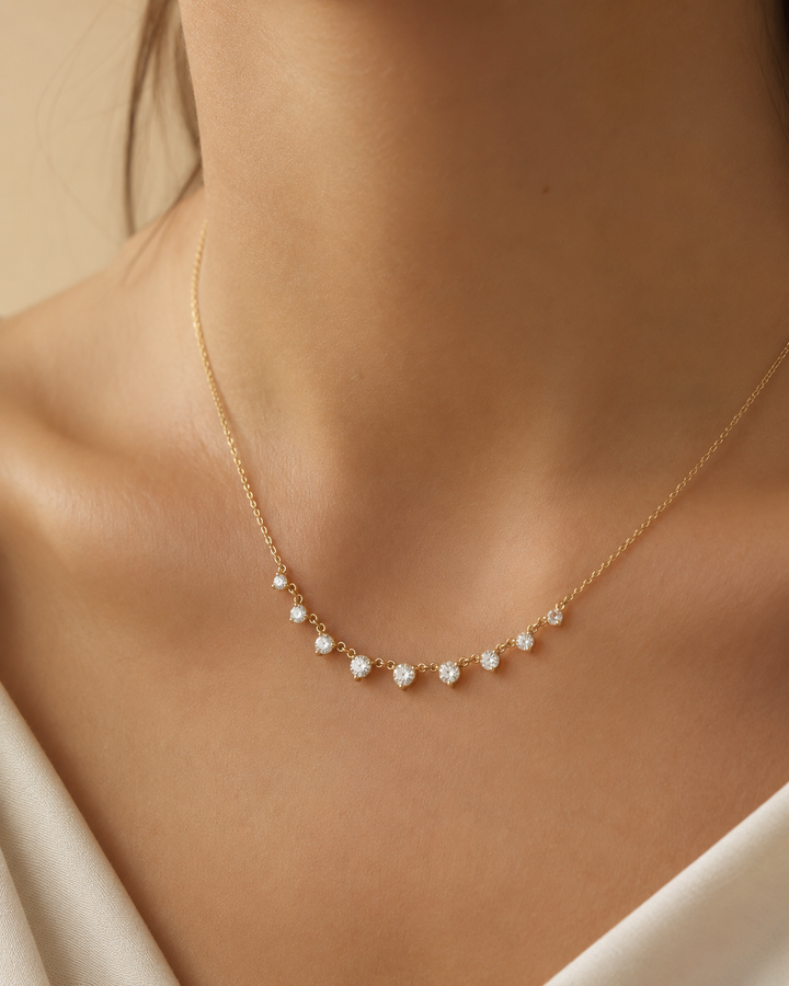 A delicate gold necklace with small white pearl-like beads and clear crystal accents, worn on a model's neck.