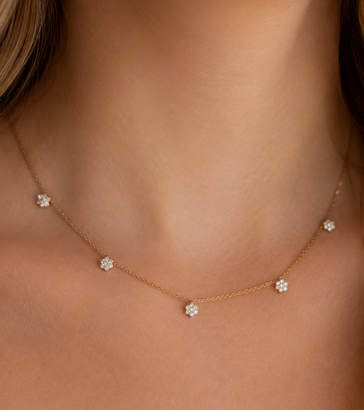 A delicate gold chain necklace with five small flower-shaped clusters of clear stones, shown worn on a model's neck.