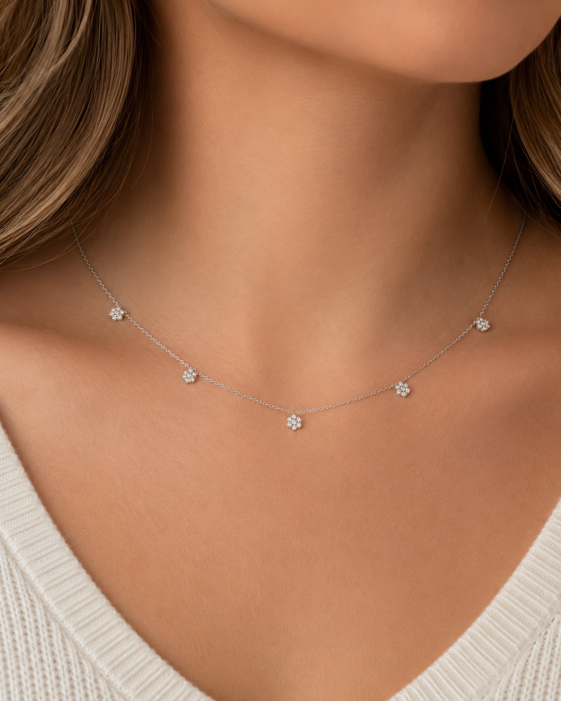 A delicate silver necklace with five small flower-shaped settings, worn on a model's neck over a white ribbed top.