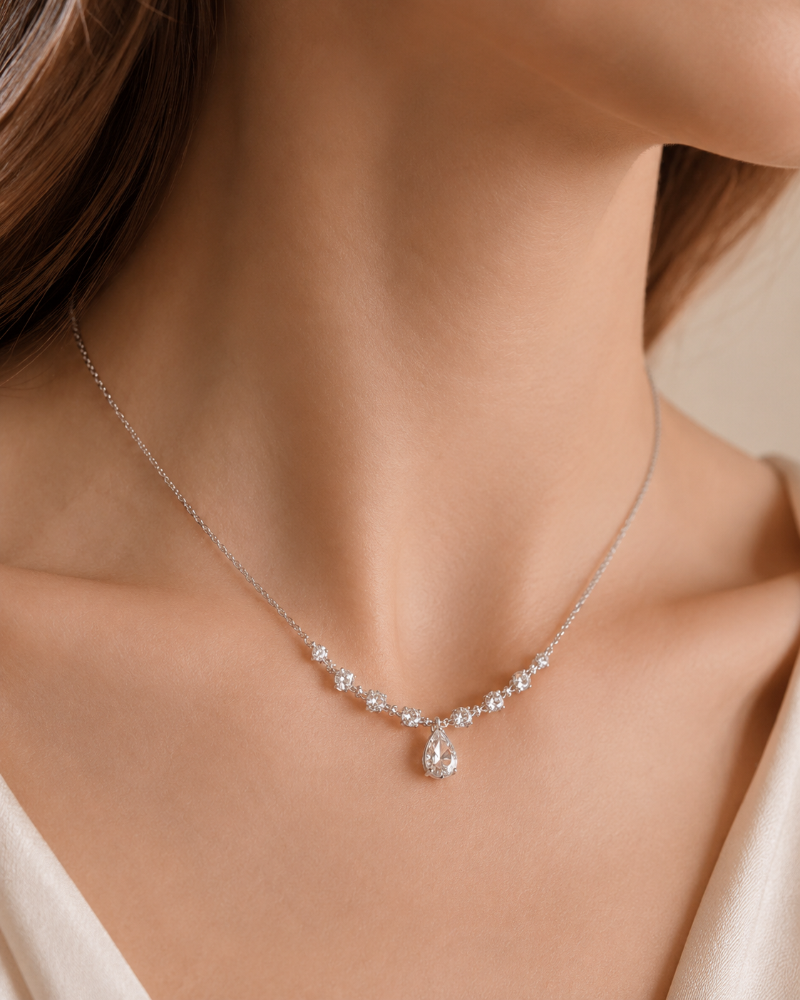 A delicate silver necklace with a teardrop-shaped clear gemstone pendant, worn on a model's neck.