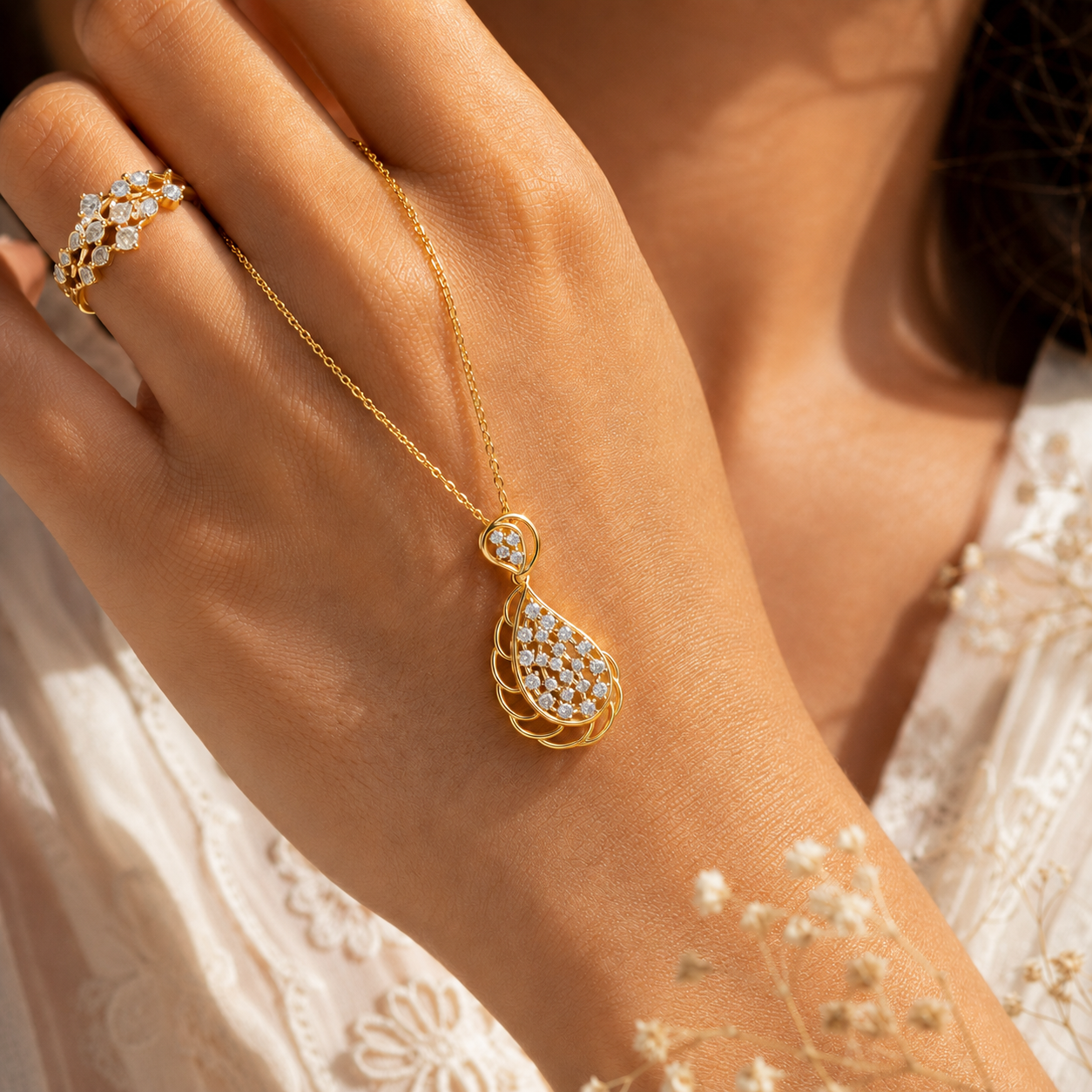 A close-up lifestyle shot of a woman's hand wearing a gold teardrop pendant necklace with clear stones and a matching gold ring.