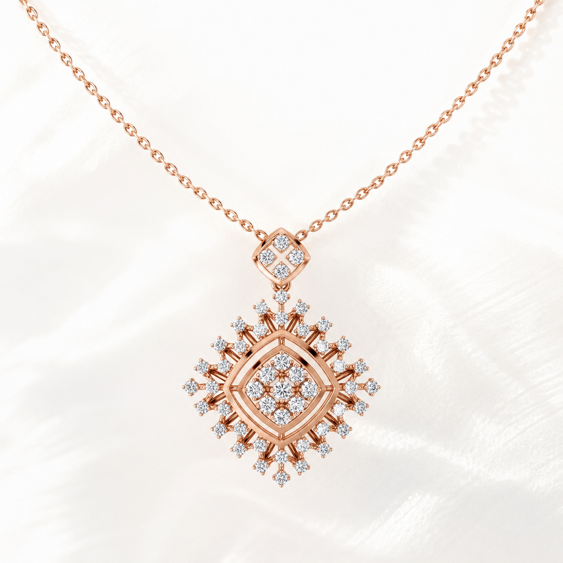 A rose gold necklace with a diamond-like pendant, displayed on a soft white fabric background. The pendant features a central diamond-shaped motif surrounded by smaller clear gemstones in a rose gold setting, with a delicate chain extending to the top corners.