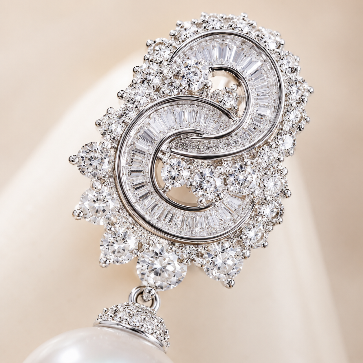 A close-up of a silver-toned double-S ring brooch embellished with clear baguette and round-cut crystals, with a dangling pearl at the bottom, set against a soft beige background.