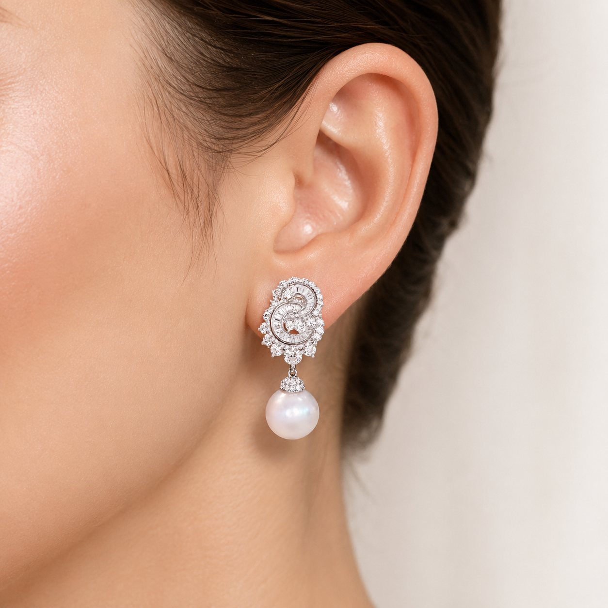 A close-up of a woman's ear wearing a silver-toned drop earring with a dangling white pearl and clear crystal detailing.