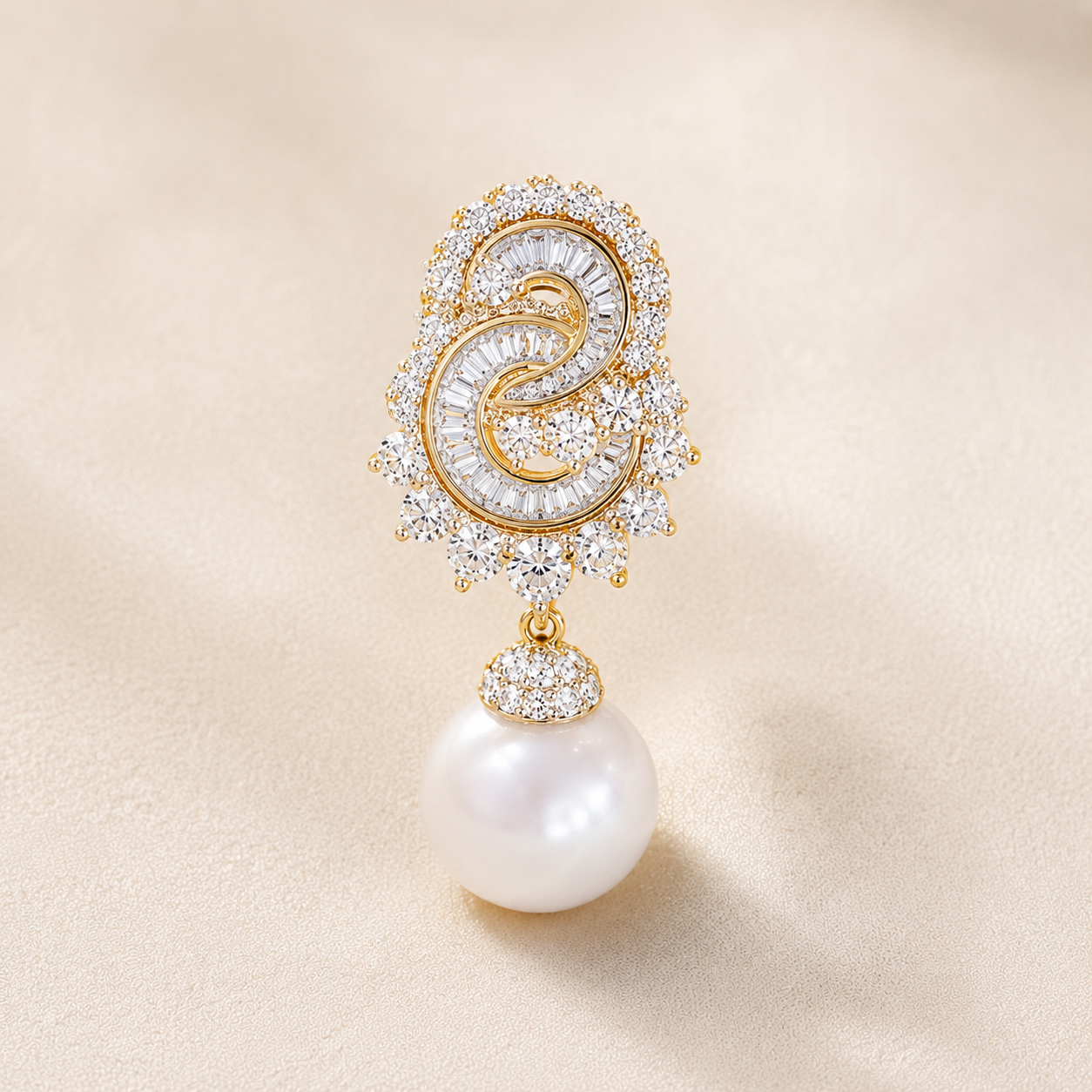 A single gold and crystal drop earring featuring a circular pavé crystal design with a central gold swirl and a dangling white pearl, set against a soft beige background.