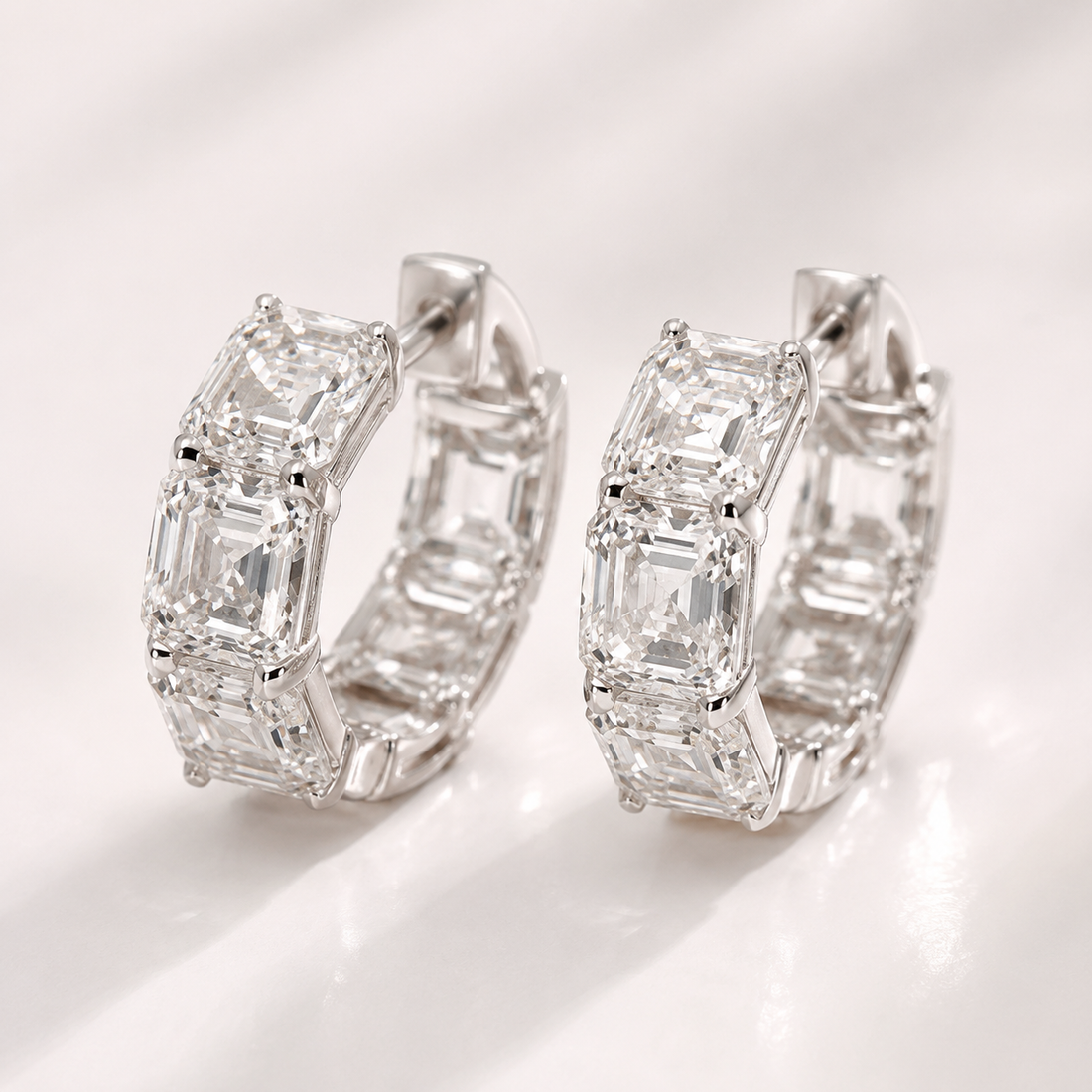 A pair of silver hoop earrings set with multiple baguette-cut clear gemstones, photographed on a clean white surface with soft shadows.