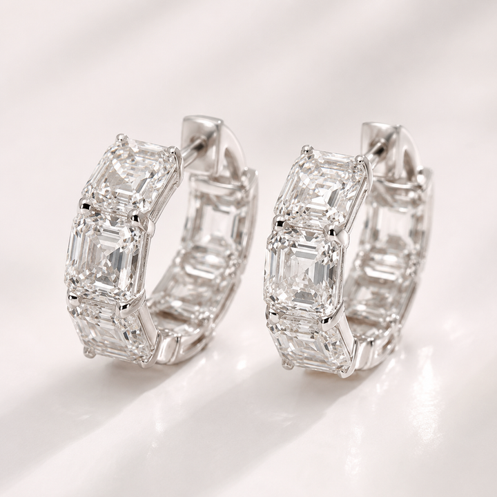 A pair of silver hoop earrings set with multiple baguette-cut clear gemstones, photographed on a clean white surface with soft shadows.