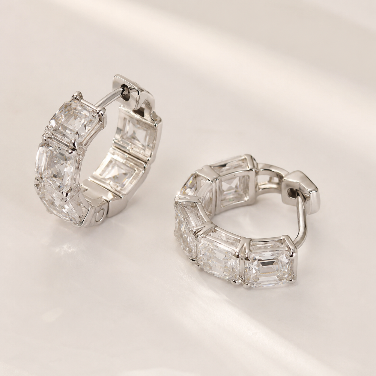 A pair of silver hoop earrings with baguette-cut clear gemstones, displayed on a clean, light-colored surface.