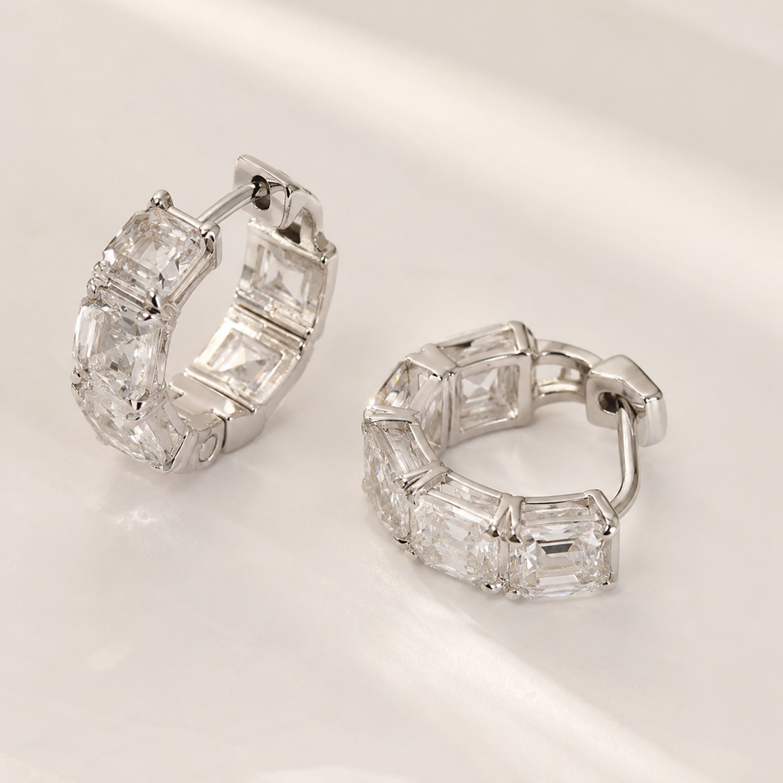 A pair of silver hoop earrings with baguette-cut clear gemstones, displayed on a clean, light-colored surface.