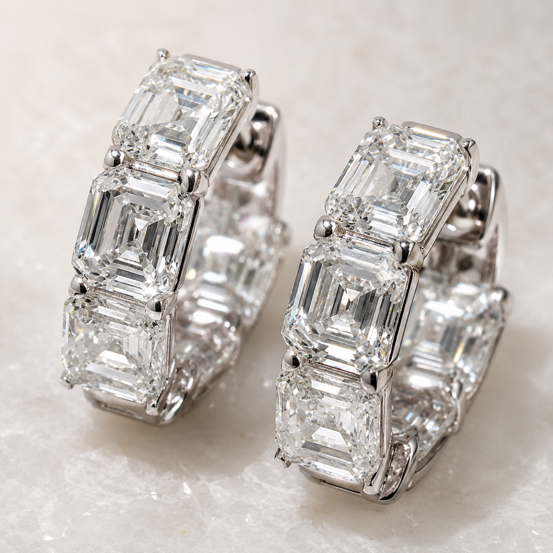 A pair of silver hoop earrings featuring a row of baguette-cut clear gemstones, displayed on a light textured surface.