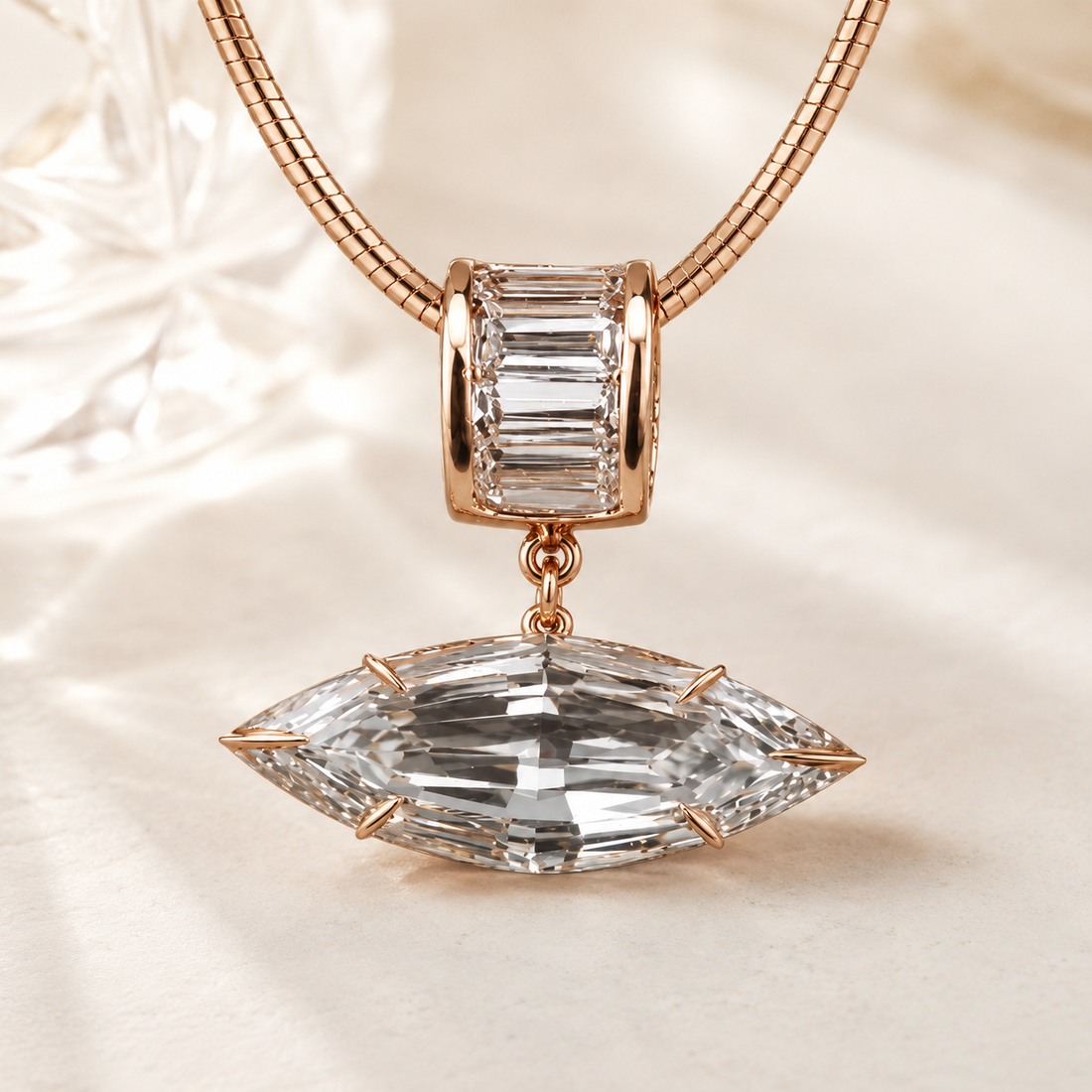 Rose gold necklace with a large marquise-cut clear crystal pendant and a smaller baguette-cut clear crystal charm, displayed on a soft cream fabric background.