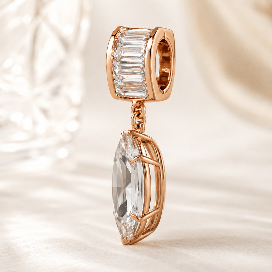 Rose gold charm bead featuring a baguette-cut clear crystal in a top setting and a larger marquise-cut clear crystal dangling below in an openwork frame, shown on a soft cream satin background.