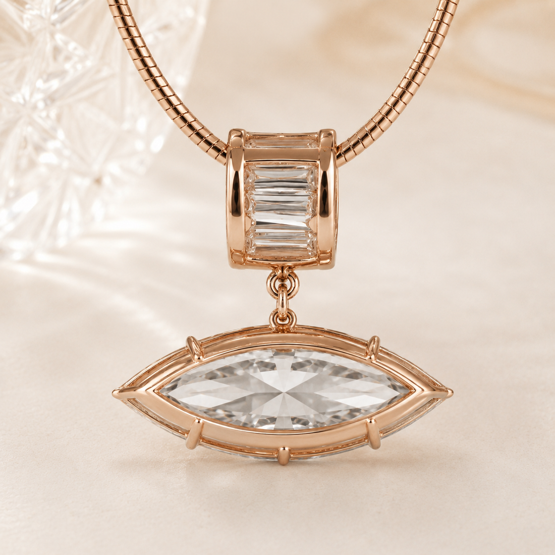 Rose gold jewelry featuring a snake chain necklace with a charm and drop pendant. The charm has a baguette-cut clear crystal, while the drop pendant is an eye-shaped marquise-cut clear crystal in a rose gold bezel setting.