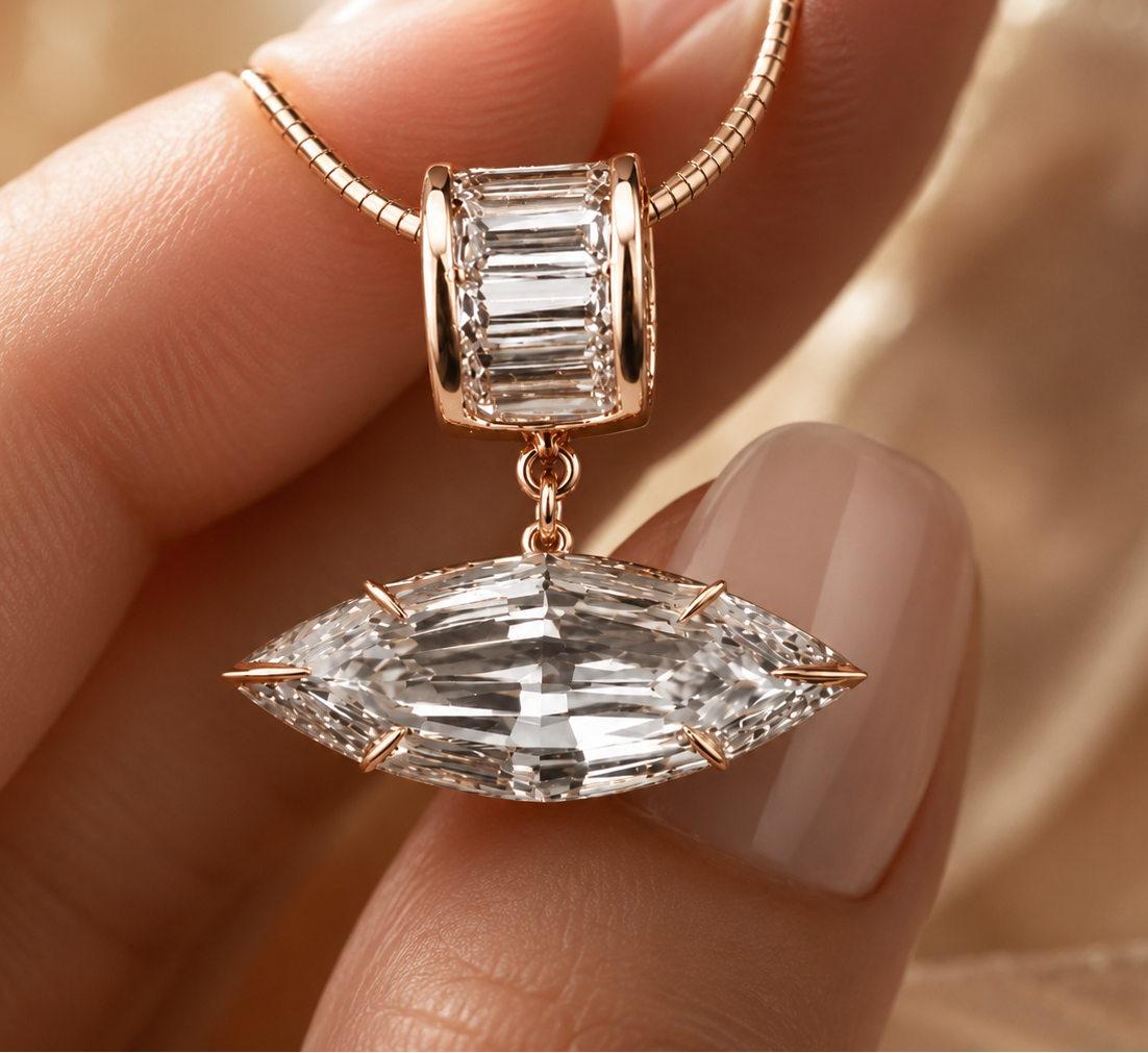 A close-up of a hand holding a rose gold charm bead with a baguette-cut clear gemstone and a dangling marquise-cut clear gemstone pendant, set against a soft beige satin background.