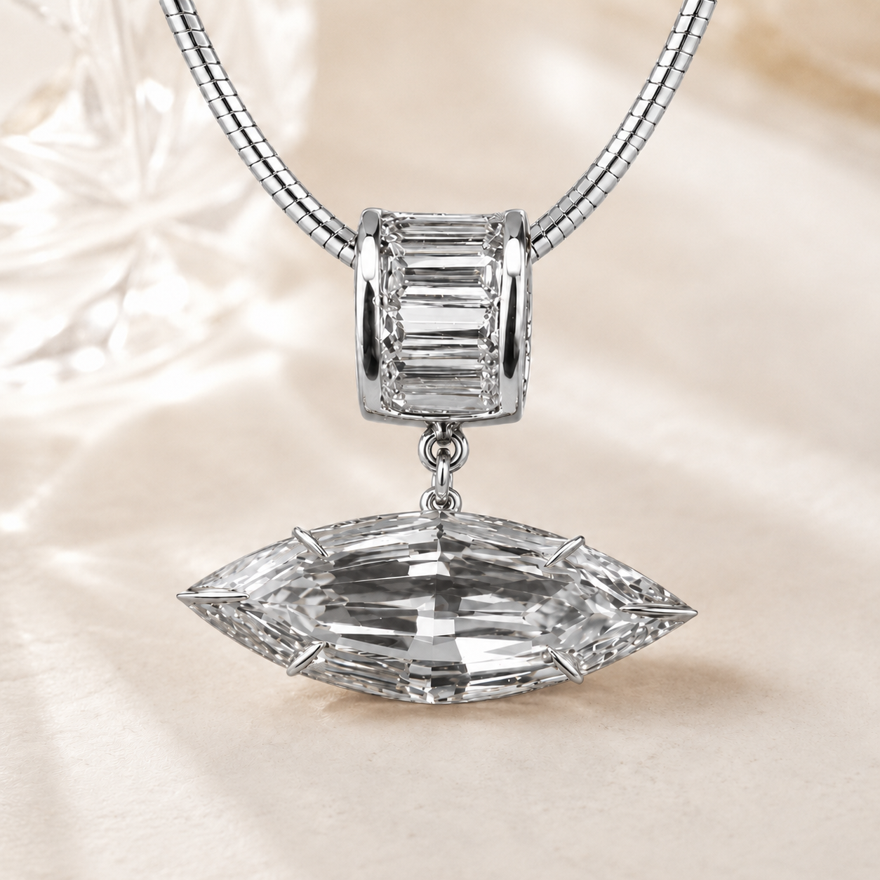 A silver-toned snake chain necklace featuring a baguette-cut crystal pendant on the clasp and a larger marquise-cut clear crystal pendant below, set against a soft cream satin background.