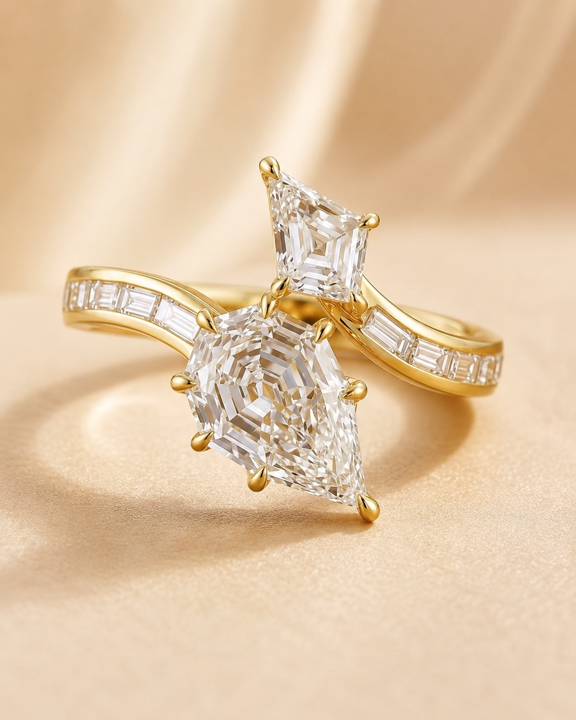 A pair of gold rings with large clear gemstones, displayed on a soft beige satin background. One ring features a pear-cut center stone, and the other features a rectangular-cut center stone, both with baguette accents on the bands.