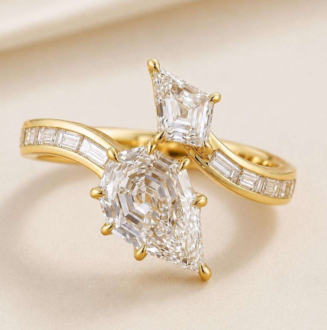 A gold ring featuring a large pear-cut clear gemstone in a prong setting, with a smaller square-cut clear gemstone above it and baguette accents along the band, photographed on a soft beige background.