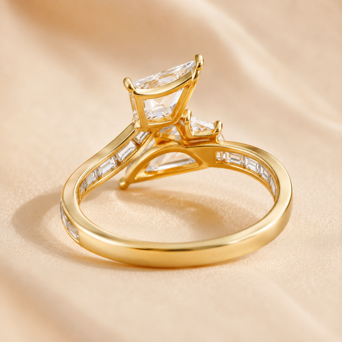 A yellow gold ring with a unique three-stone cluster setting featuring clear baguette and round-cut stones, resting on a soft beige satin fabric background.
