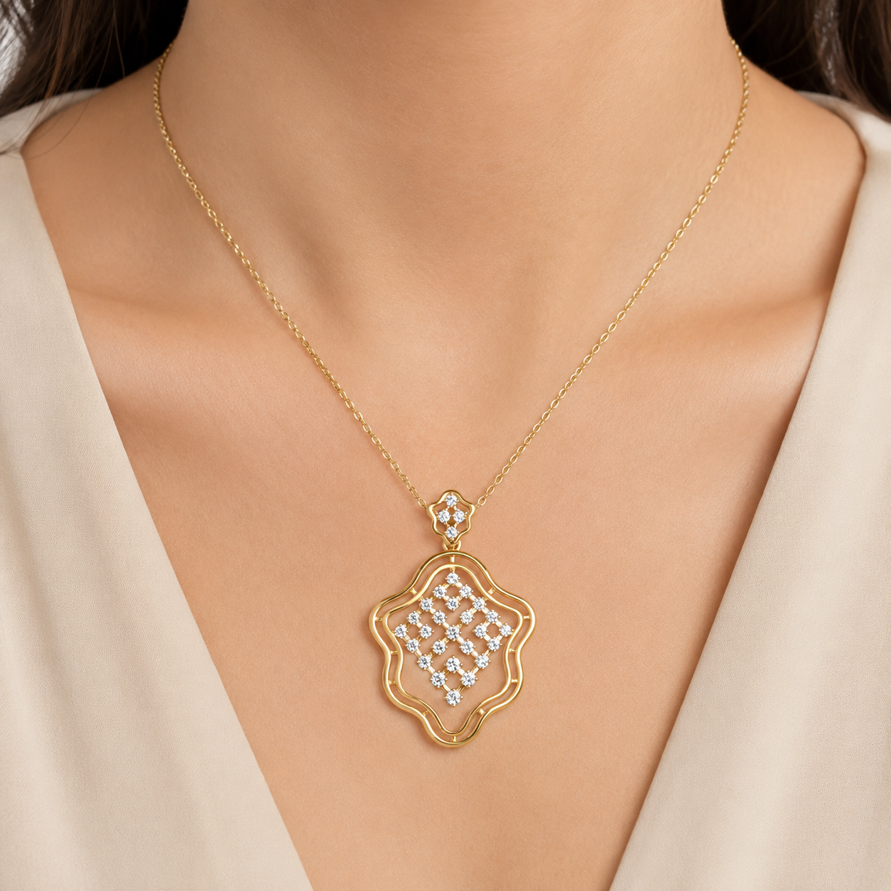A gold necklace with a scalloped, openwork pendant set with clear rhinestones, worn on a model's neck over a cream-colored top.