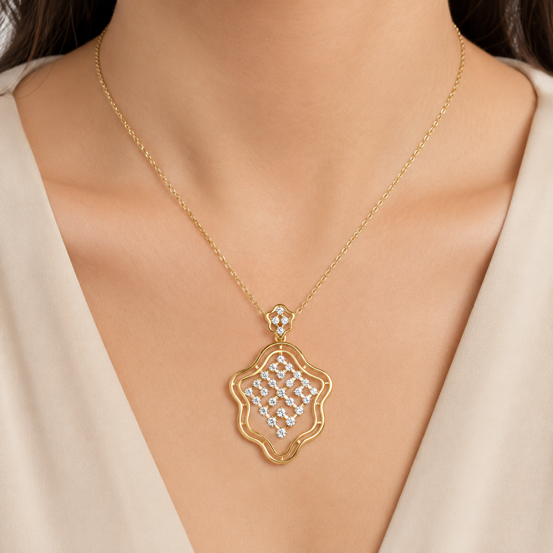 A gold necklace with a scalloped, openwork pendant set with clear rhinestones, worn on a model's neck over a cream-colored top.