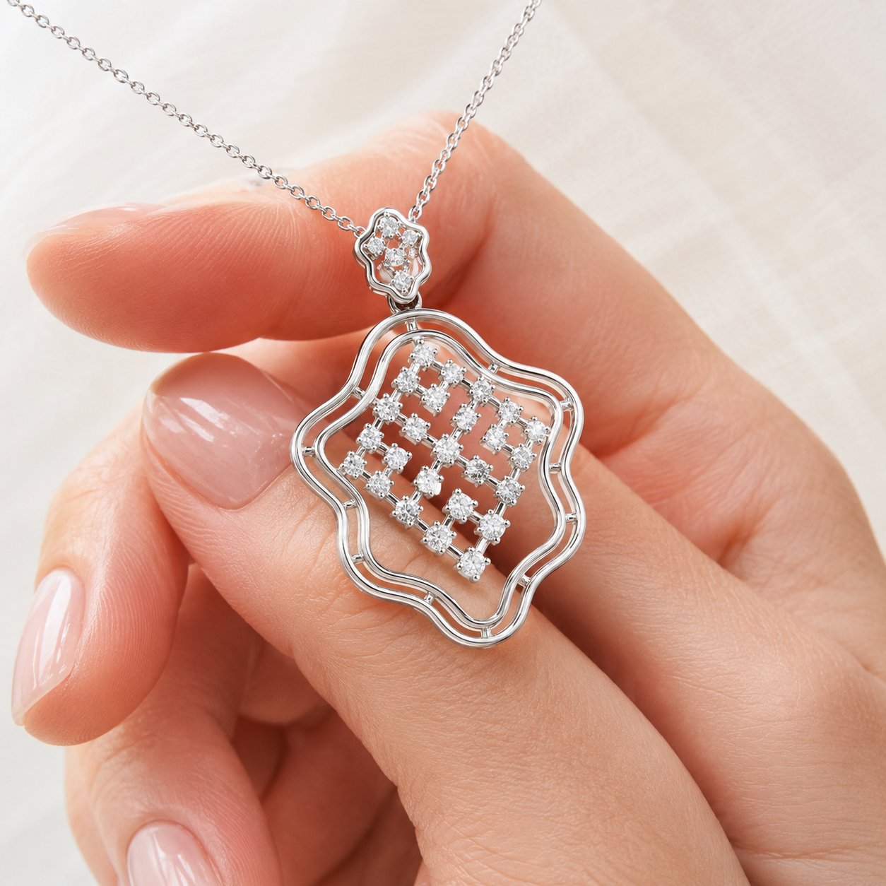 A silver-toned necklace with a decorative openwork pendant and clear gemstones, held in a person's hand against a soft light background.