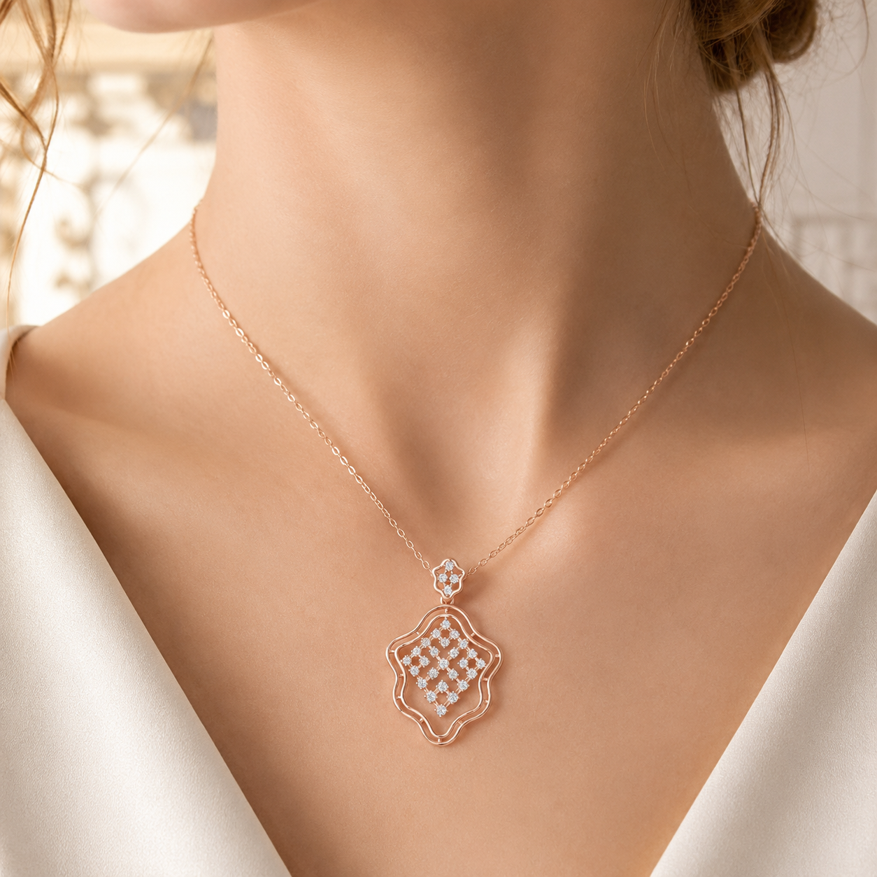 A close-up of a model's neck and chest wearing a delicate rose gold necklace with a geometric pendant studded with small clear crystals.