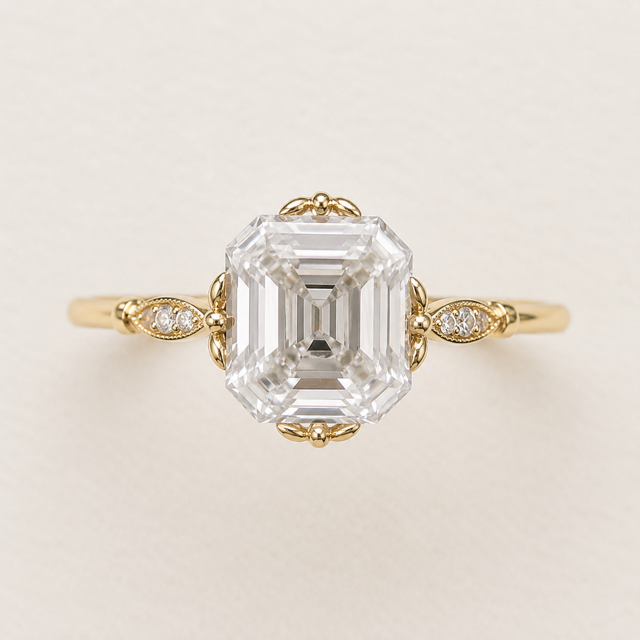 An emerald-cut diamond engagement ring in yellow gold, featuring a large central diamond and smaller accent diamonds on the band, set against a plain light beige background.