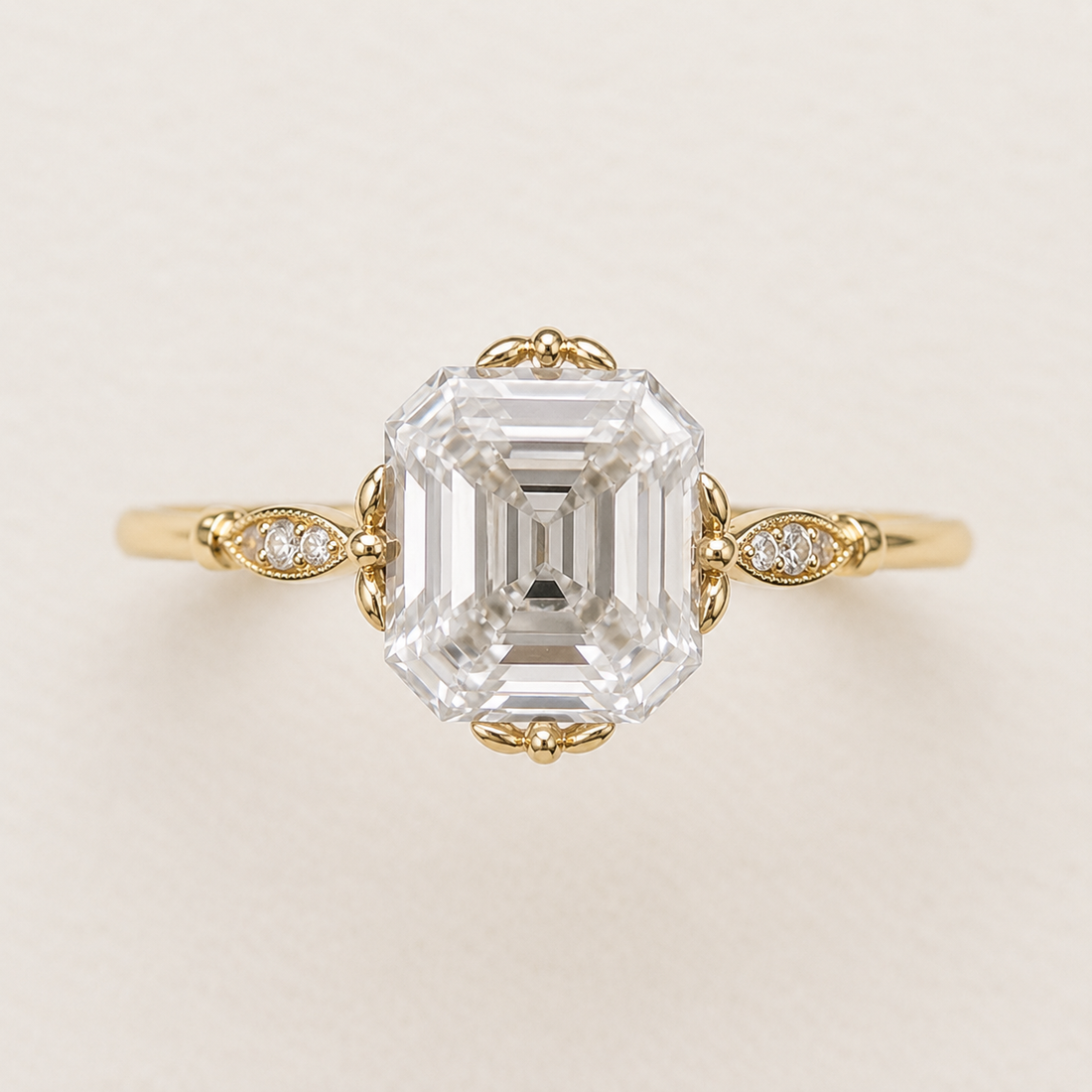 An emerald-cut diamond engagement ring in yellow gold, featuring a large central diamond and smaller accent diamonds on the band, set against a plain light beige background.