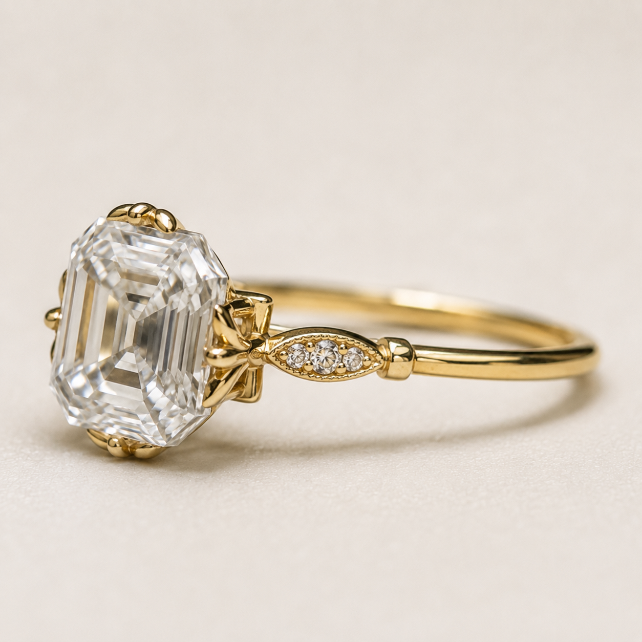 A yellow gold ring featuring a large emerald-cut clear gemstone and a small diamond-accented leaf motif on the band, set against a neutral light beige background.