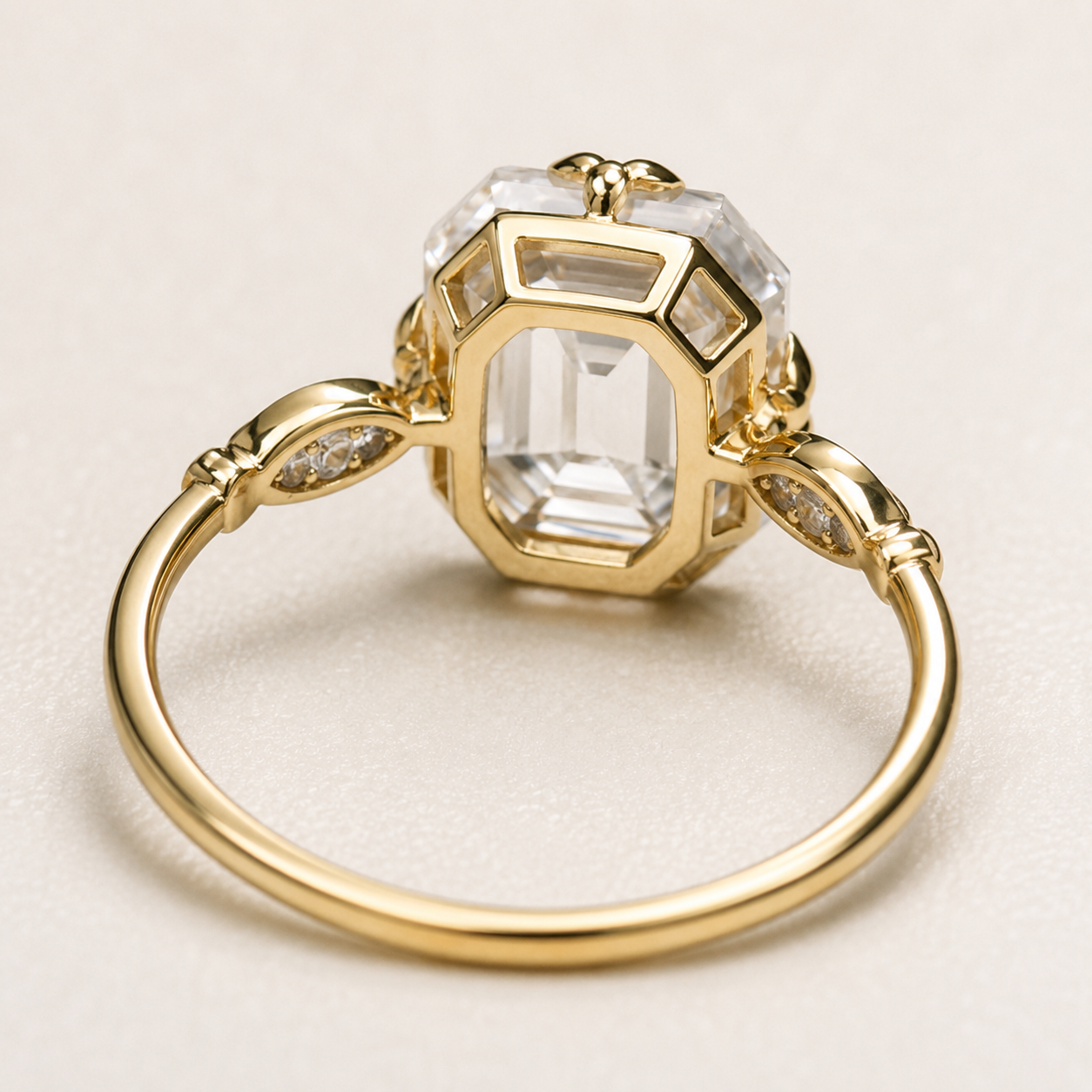 A gold ring with a large clear emerald-cut center stone and smaller clear stones along the band, photographed on a light neutral background.