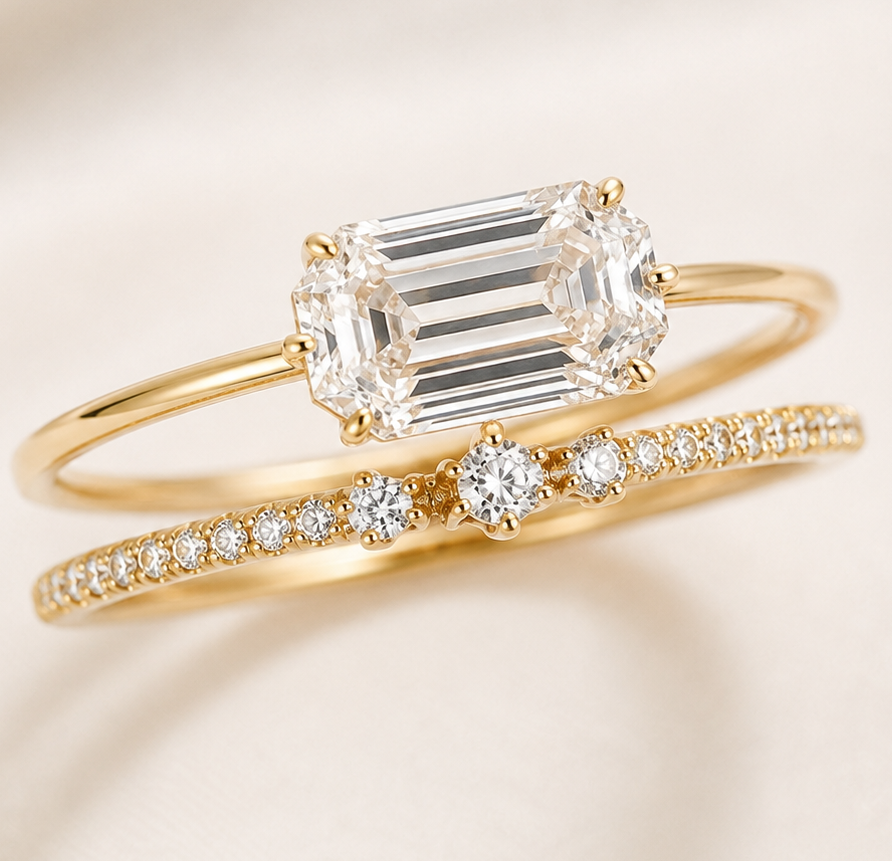 A gold ring set featuring a yellow gold engagement ring with an emerald-cut clear center stone and a matching yellow gold wedding band with pavé-set clear stones, displayed on a soft cream-colored fabric background.
