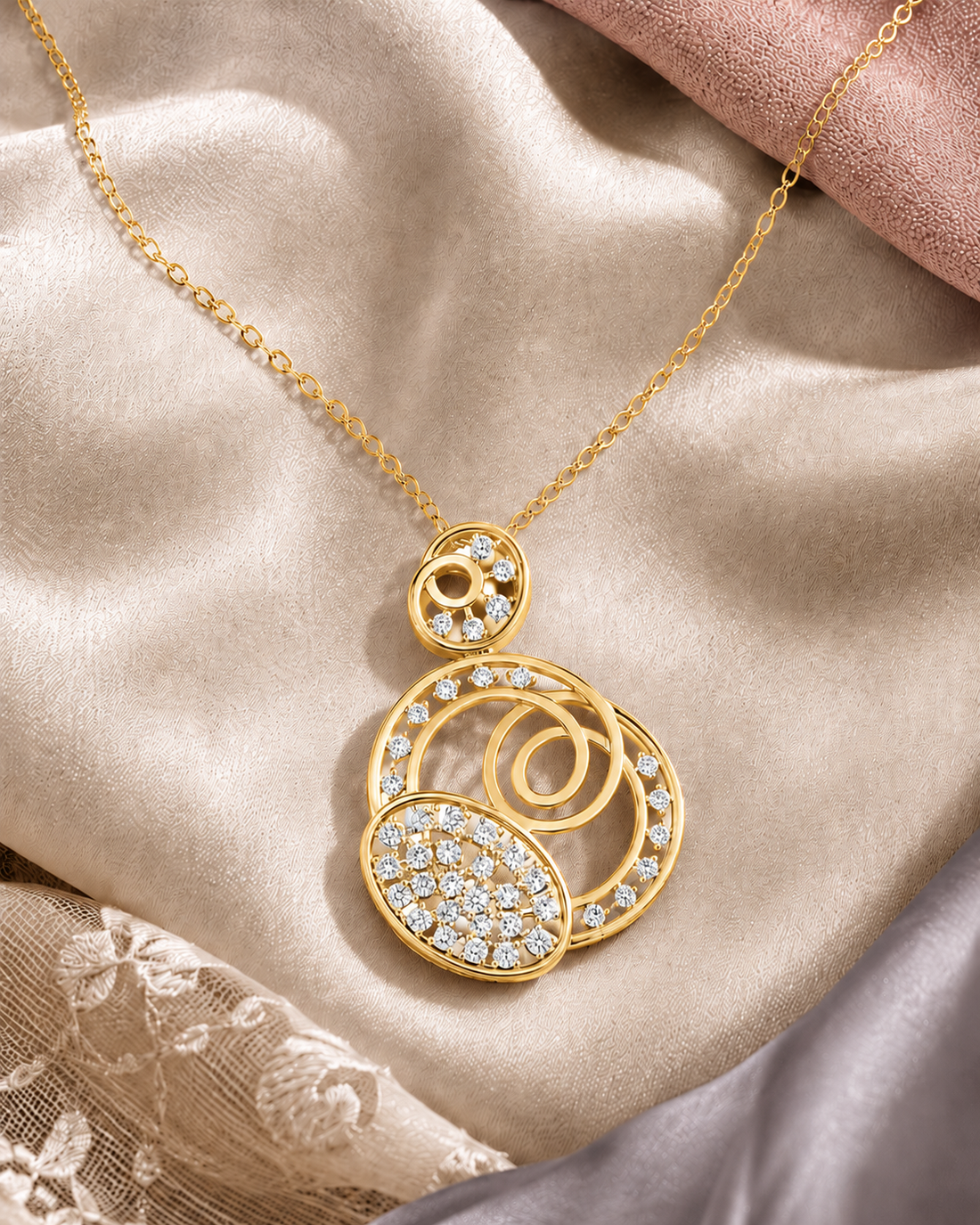 A gold pendant necklace with a multi-layered abstract design set with clear pavé and round crystals, displayed on a draped beige satin fabric.